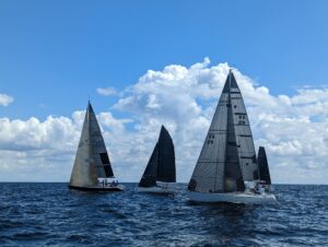Photo of several racing sailboats with black and gray sails competing in a race.